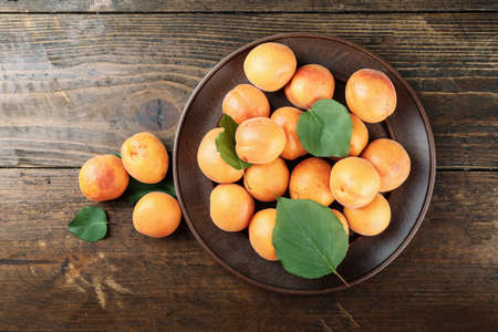 Ripe apricots with leaves in a clay plate on a wooden background. space for textの写真素材