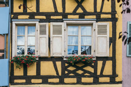 facade with windows with shutters in the old house. flowers grow in pots by the windowsの写真素材