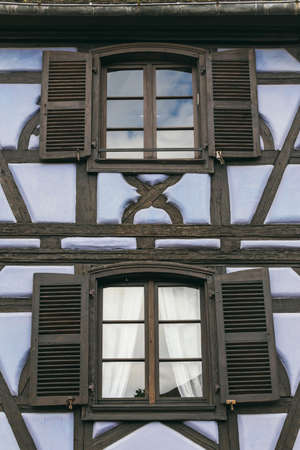 facade with windows with shutters in the old house. flowers grow in pots by the windowsの写真素材