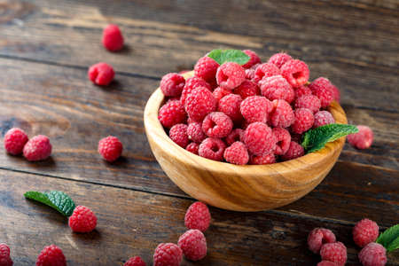 Fresh raspberries in a wooden plate on a brown wooden background. close-up. place for text. raspberry texture is clearly visibleの写真素材