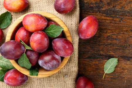 ripe red plum in a plate on a burlap on a shabby wooden background. place for text.の写真素材