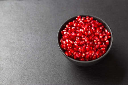 grains of pomegranate fruit in a plate on a black background. space for textの写真素材