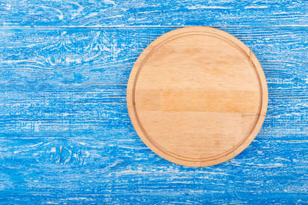 Round pizza cutting board on a blue wooden background. space for textの写真素材