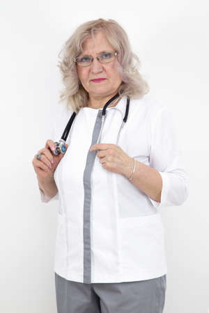 elderly female doctor with a stethoscope and in uniform against a white wallの写真素材