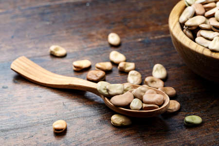 dry large beans in a wooden spoon against a brown wooden background. space for text