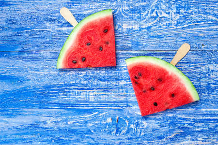 watermelon cut into a triangle shape with a stick on a fresh blue wooden backgroundの写真素材