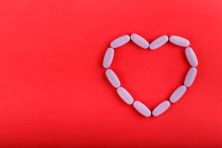 oval pink pills laid out in the shape of a heart on a bright red background. space for text