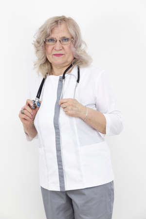 elderly female doctor in modern medical uniform with a stethoscope standing by the white wallの写真素材