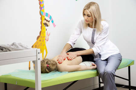 girl doctor does massage to a child girl. the girl is lying on the couch in the doctor's officeの写真素材