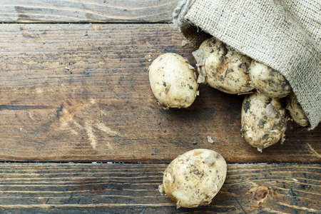 Fresh potatoes in an old sack on wooden background. Top viewの写真素材