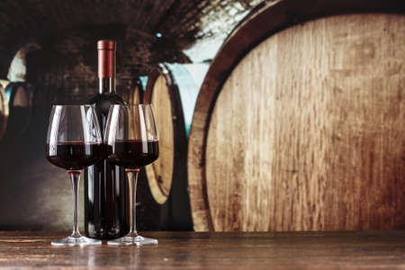 red wine in a glass against the background of large barrels in the cellarの写真素材