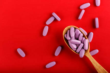 pink pills in a wooden spoon on a red background. place for textの写真素材