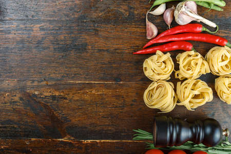 uncooked tagliatelli spaghetti on a brown wooden background. set with vegetables. place for textの写真素材