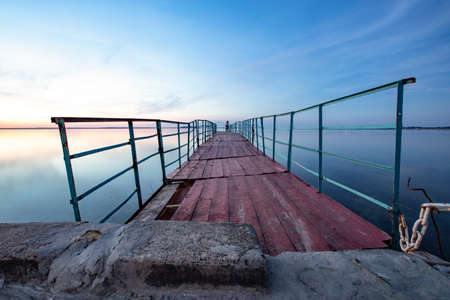 old wooden pier on the sea. stones in the foreground. at the end of the pier you can see a coupleの写真素材