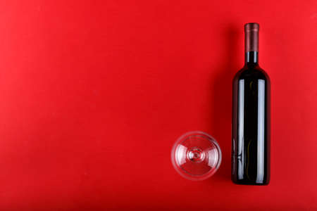 a bottle of red wine without a label, next to an empty glass, on a red background. place for text
の写真素材