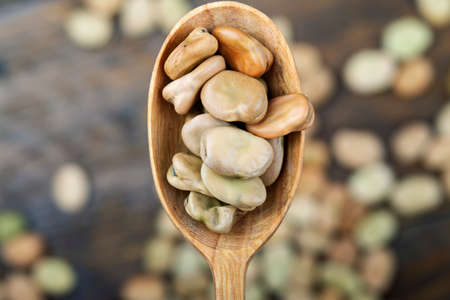 raw broad beans in a wooden spoon on a brown wooden background. place for textの写真素材