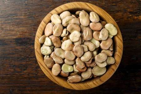 raw broad beans in a wooden plate on a wooden background. place for text. bean texture clearly visibleの写真素材