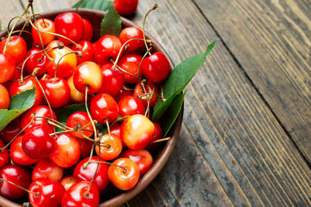 Fresh harvest of sweet cherries in a clay bowl on a wooden table. Healthy fruits.の写真素材