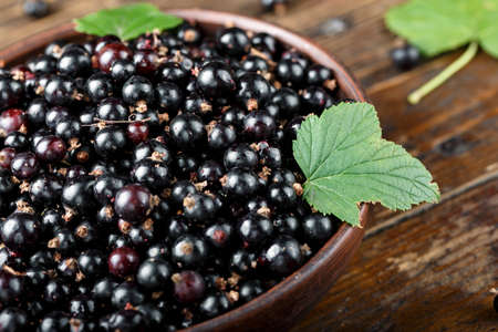 fresh currant with green leaves in a clay plate on a brown wooden table. harvest of vitamin berries