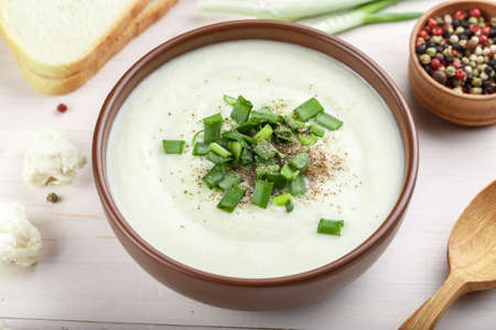 White vegetable cream soup of cauliflower in a brown clay plate on a wooden background. Simple diet dish.の写真素材