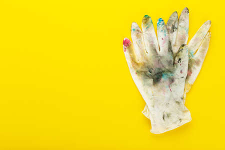 White rubber gloves in spots of paint on yellow background. Place for text. The concept of...