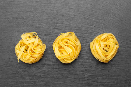 uncooked pasta nests lie in a row on a black background. place for textの写真素材