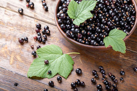 ripe organic currants with green leaves in a clay plate, on a wooden background. clearly visible...