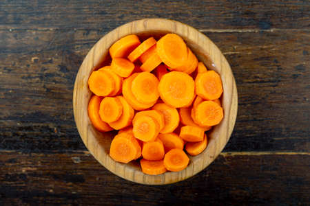 sliced raw carrots in a plate on a brown wooden background. view from aboveの写真素材