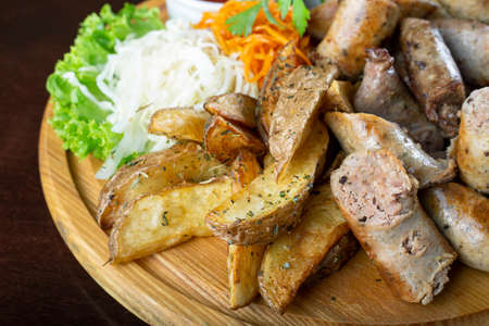 Homemade grilled sausages with sauerkraut and ketchup on a round wooden tray. Beer snacks.