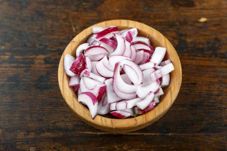 Sliced raw red onion in a bowl on a wooden background. Vegetable, ingredient and staple food. Healthy food.の写真素材