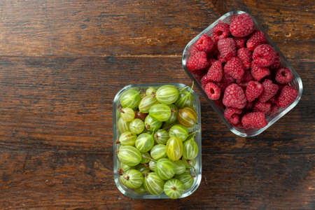Assorted berries of raspberries, gooseberries in glass bowls on a wooden table. Top view.の写真素材