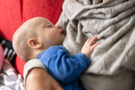 Beautiful baby in blue pajamas sleeping in mom's armsの写真素材