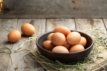 Fresh chicken eggs in a clay bowl on the hay. Rural scene.