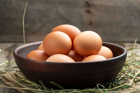 Fresh chicken eggs in a clay bowl on the hay. Rural scene.