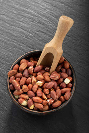Peeled peanuts in a clay bowl on a black table.