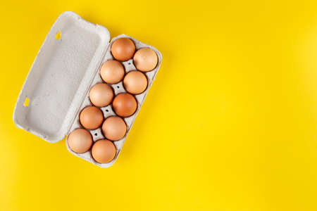 Chicken eggs in an open egg carton isolated on yellow. Top view with copy space. Natural healthy food and organic farming concept.の写真素材