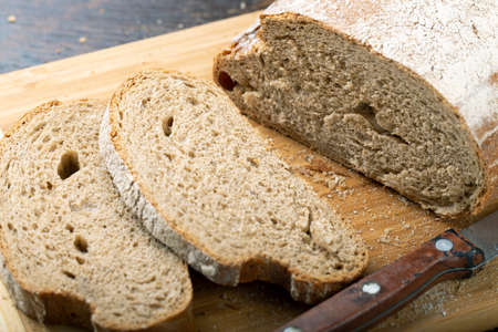 Fresh bread slice and cutting knife on rustic table