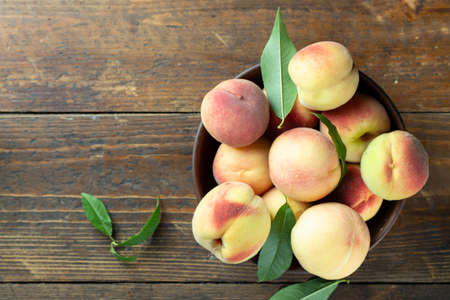 Ripe peaches with leaves in a clay bowl on a wooden table. Fresh harvest. Top view.の写真素材