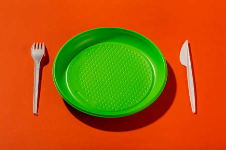 Plastic set of disposable tableware consisting of a plate, knife and fork on an orange background.の写真素材