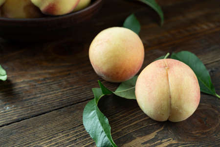 Fresh harvest of peaches in a clay bowl on a wooden rustic table. Peach leaves are present in the composition. Organic fruit, vegan food.の写真素材
