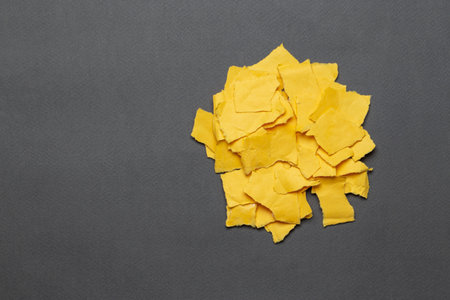 Pile of torn yellow paper scraps on a gray background. Space for text. Top view.