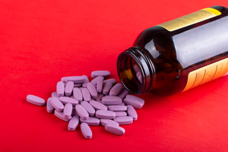 oval pink pills are poured from a jar on a bright red background. space for textの写真素材