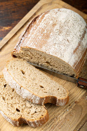 Fresh bread slice and cutting knife on rustic table