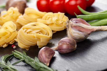 Raw pasta tagliatelle with fresh tomatoes, peppers, mushrooms, asparagus beans, spices and cheese on black table. Food ingredients for Italian spaghetti.の写真素材