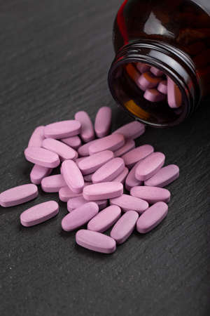 Pink pills are scattered from a glass jar on a black background. Health care concept. Space for...