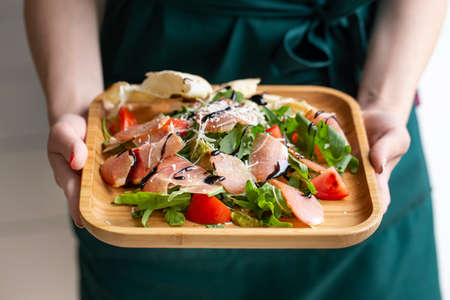 Fresh salad and arugula, bacon, tomatoes sprinkled with parmesan cheese. Hands of waiters close up.