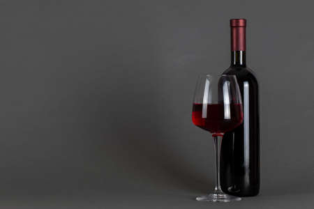 Red wine bottle and glass on a gray background. Wine drinking culture concept. Space for text.の写真素材