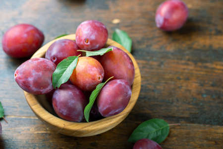 Ripe plums and leaves in a wooden bowl on the table. Harvesting season.の写真素材