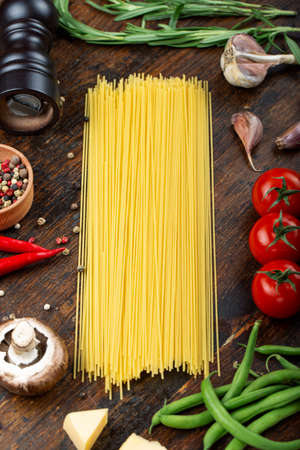 Raw pasta with fresh tomatoes, peppers, asparagus beans, spices and cheese on a wooden table. Food ingredients for Italian spaghetti.の写真素材