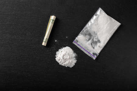 Cocaine in a plastic package on a black background, close-up. A rolled up dollar bill for drug use....